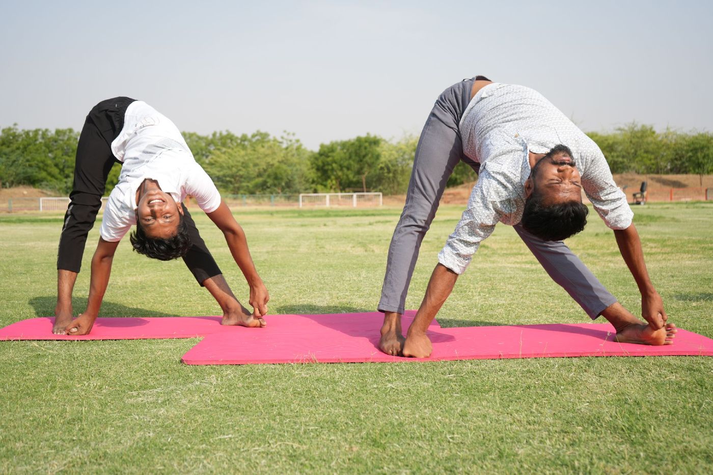 Navpratap and a partner in a wide-legged standing forward bend on pink mats