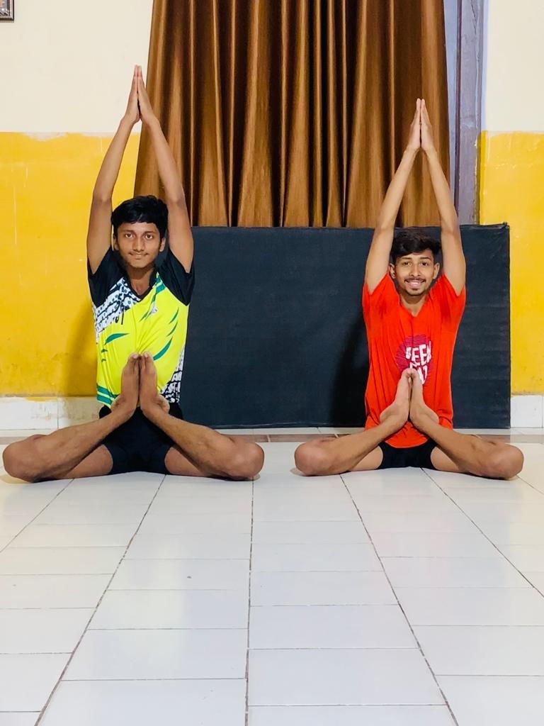Two practitioners seated with hands overhead in a namaste pose